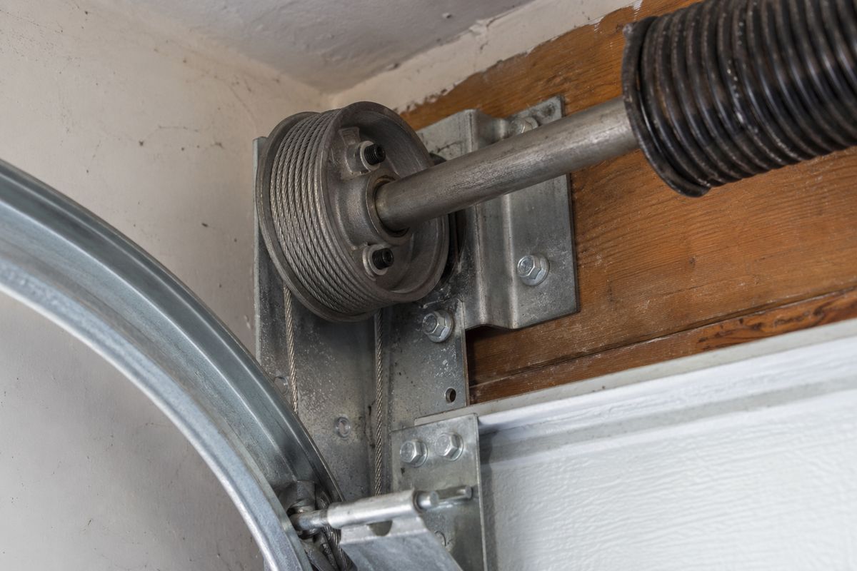 Garage door cable drum on the torsion shaft, lift cable wound into its grooves, spring alongside