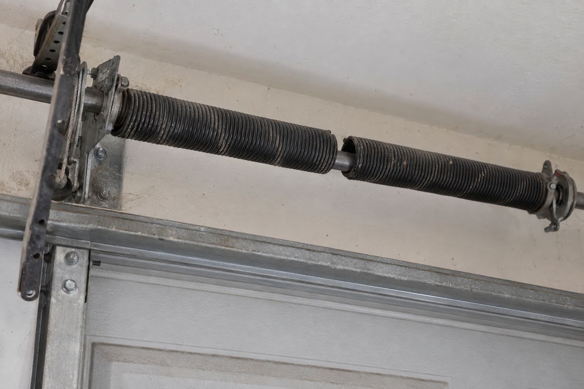 Broken garage door torsion spring above the door, with a clear gap where the coil has snapped
