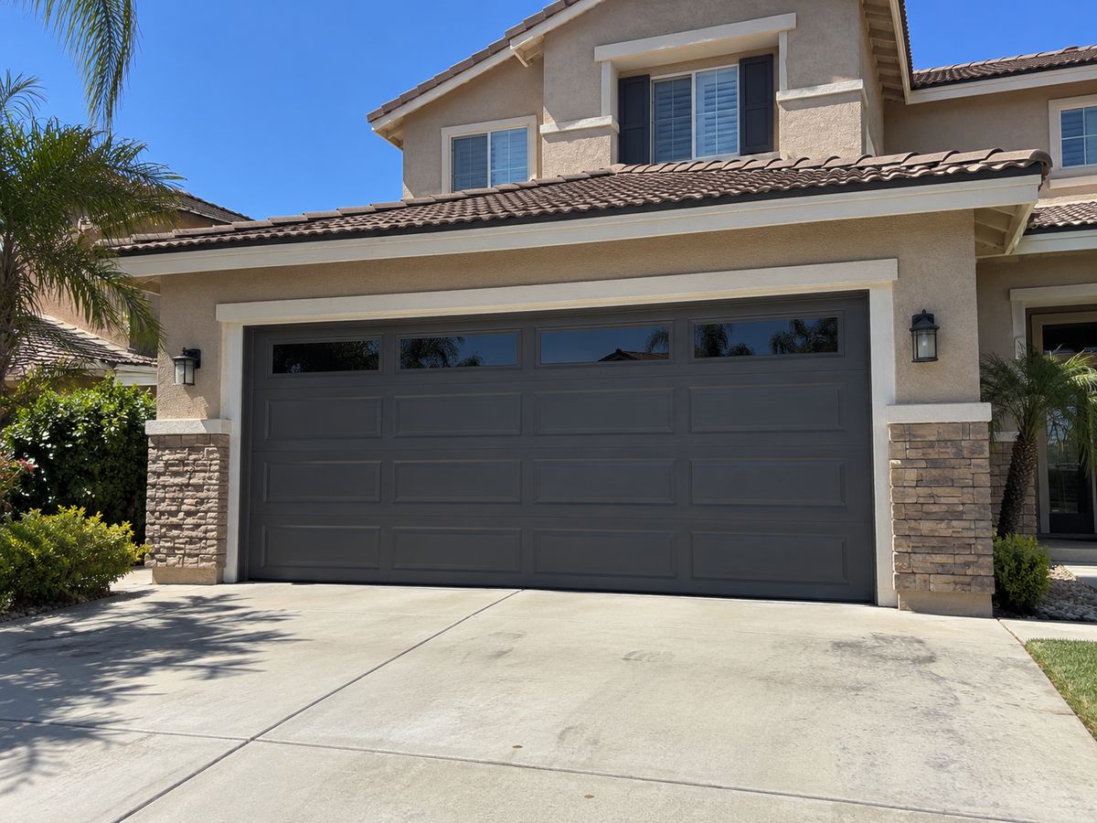 Charcoal garage door with a window row between stone-clad pillars on a two-story home
