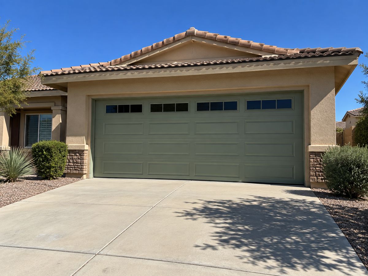 Sage green long-panel garage door with windows on a tile-roofed home with desert landscaping