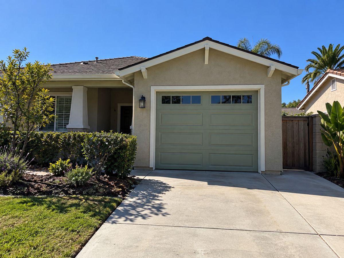 Single-car sage green garage door with windows on a small cottage-style home with a front garden
