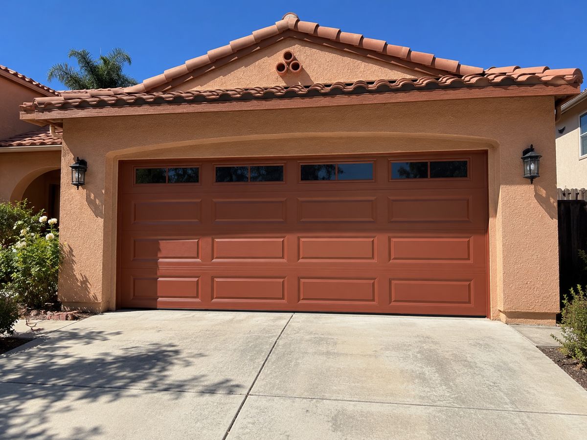 Terracotta-red raised-panel garage door with windows on a Spanish-style home with a clay tile roof