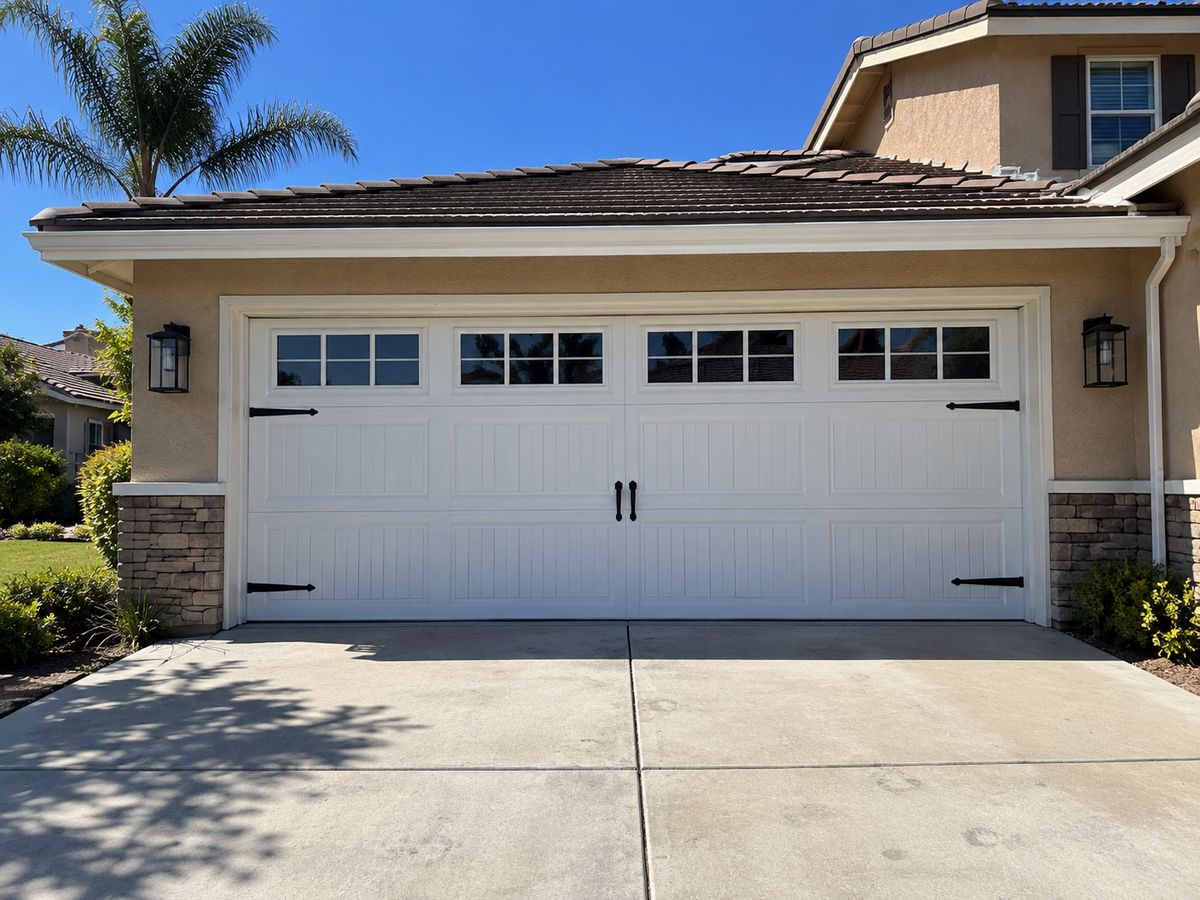 White carriage-house style garage door with a window row and black decorative hinges and handles