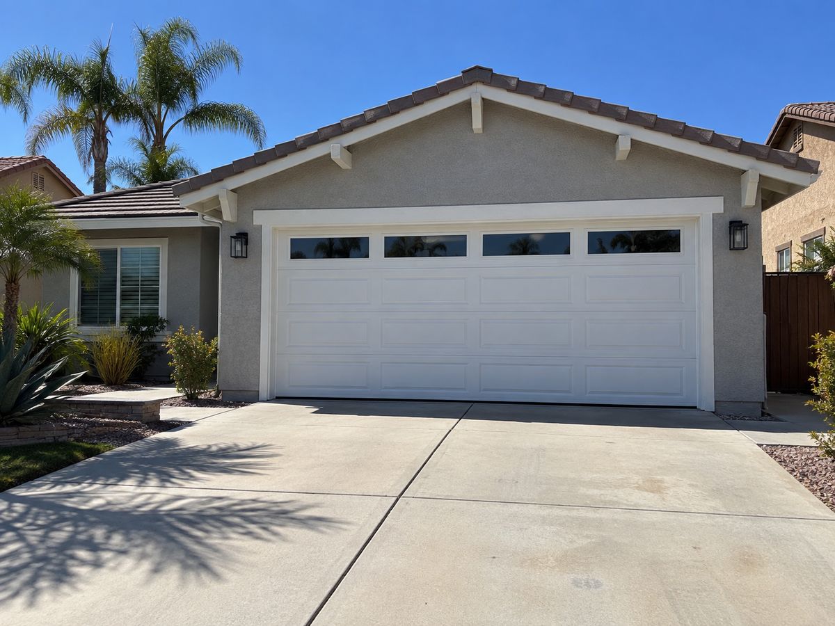 White long-panel double garage door with a row of windows on a single-story stucco home with palm trees