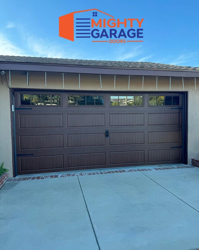 Dark brown carriage-house garage door with a window row and black strap handles on a home with horizontal siding