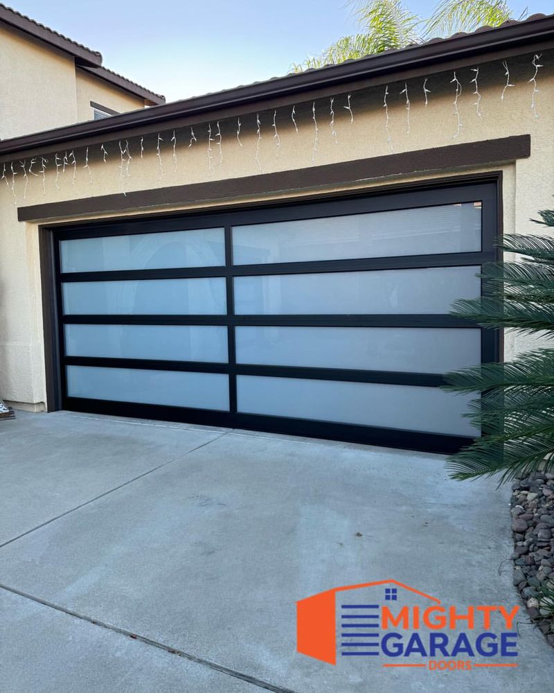 Full-view garage door with a dark aluminum frame and frosted glass panels on a single-story home