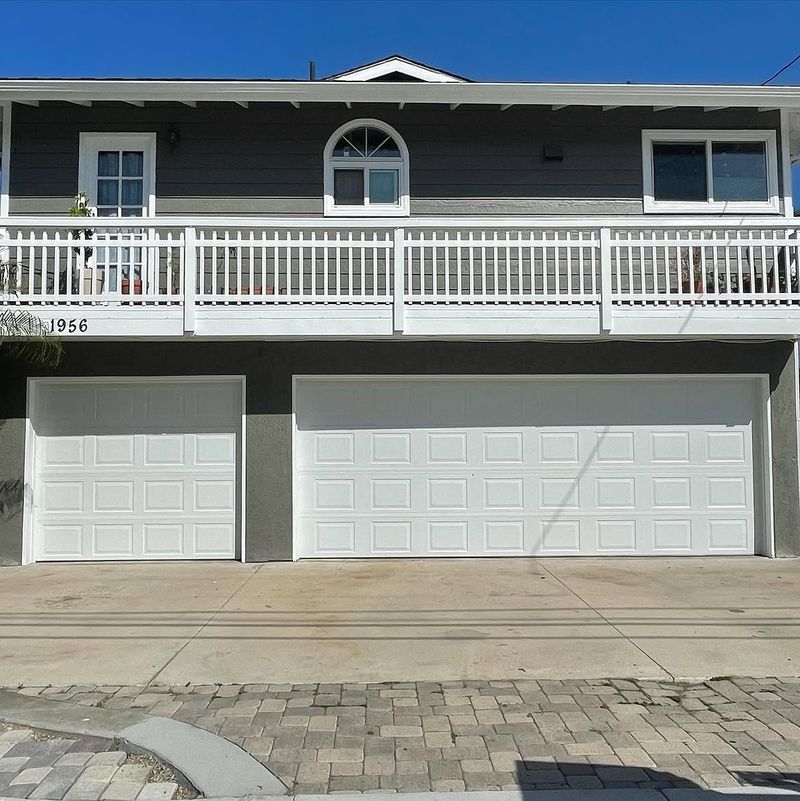 One single and one double white garage door on a gray two-story Newport Beach home with a deck above