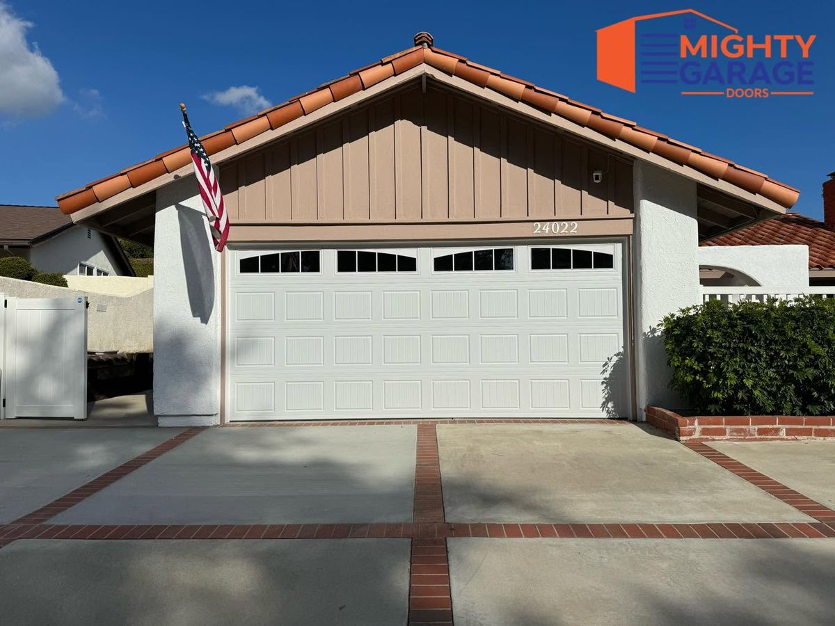 White raised-panel double garage door with a window row on a home with a red tile roof and brick-trimmed driveway