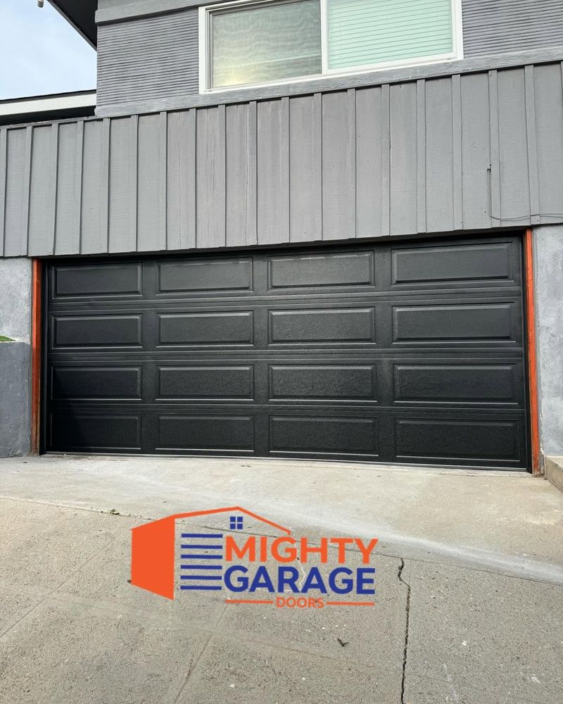 Black long-panel double garage door on a home with gray vertical board siding above the opening
