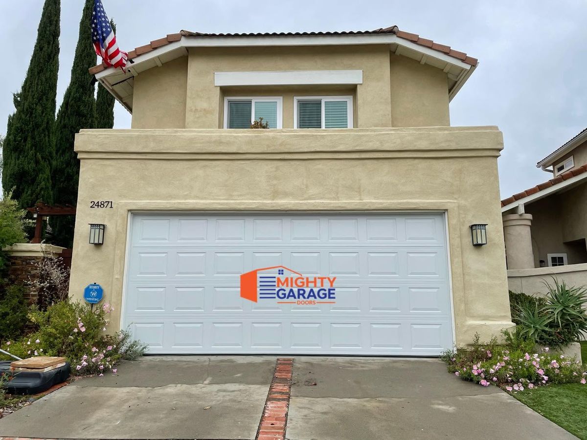 White raised-panel double garage door on a two-story stucco home with an American flag and brick-trimmed driveway
