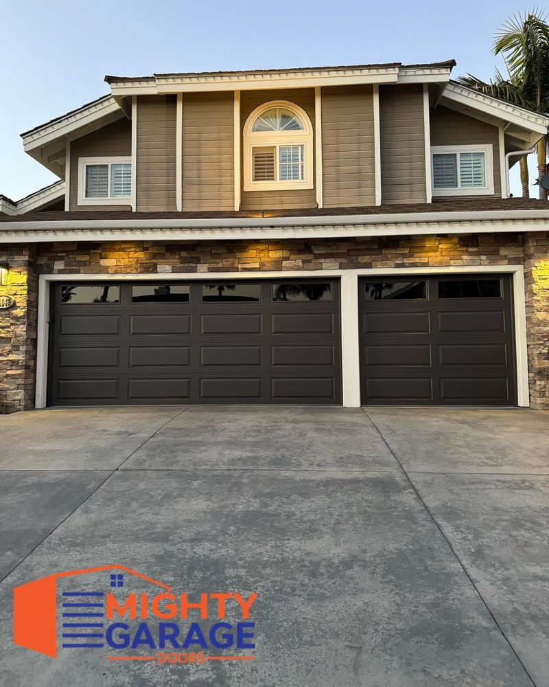 Dark brown double garage door and matching single door on a two-story home with stone veneer, lit at dusk