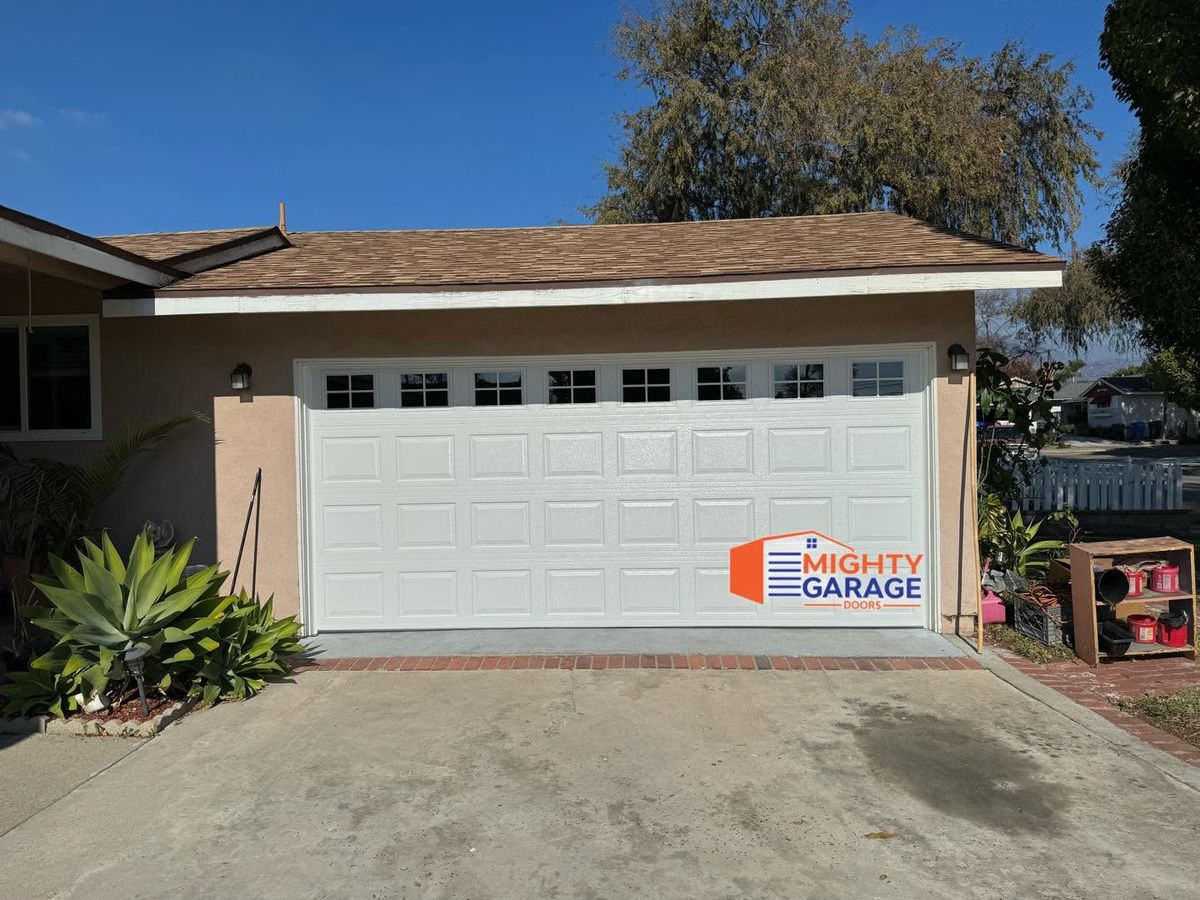 White raised-panel double garage door with a window row on a single-story home with agave beside the driveway