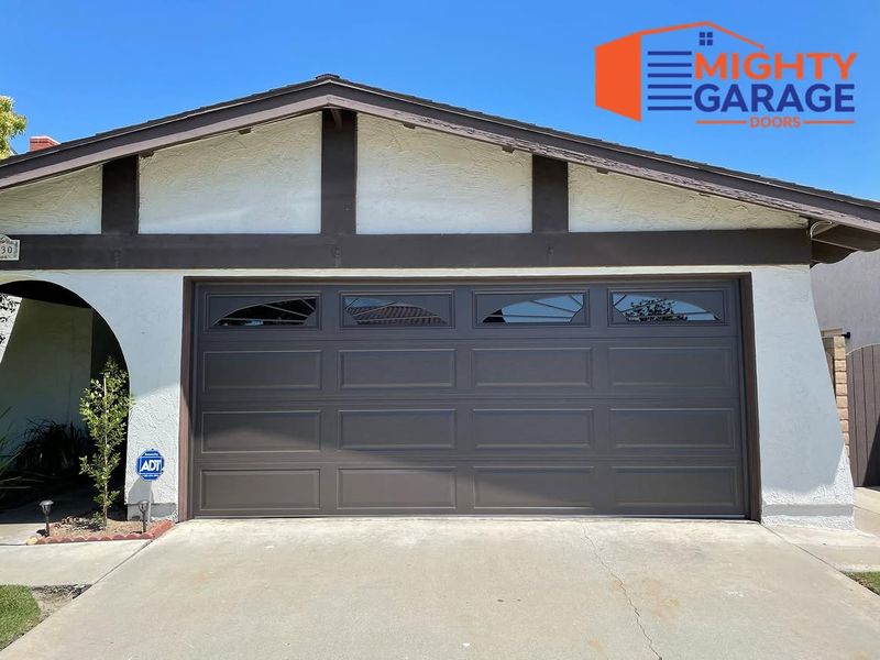Dark brown long-panel double garage door with a window row on a single-story home with exposed roof beams