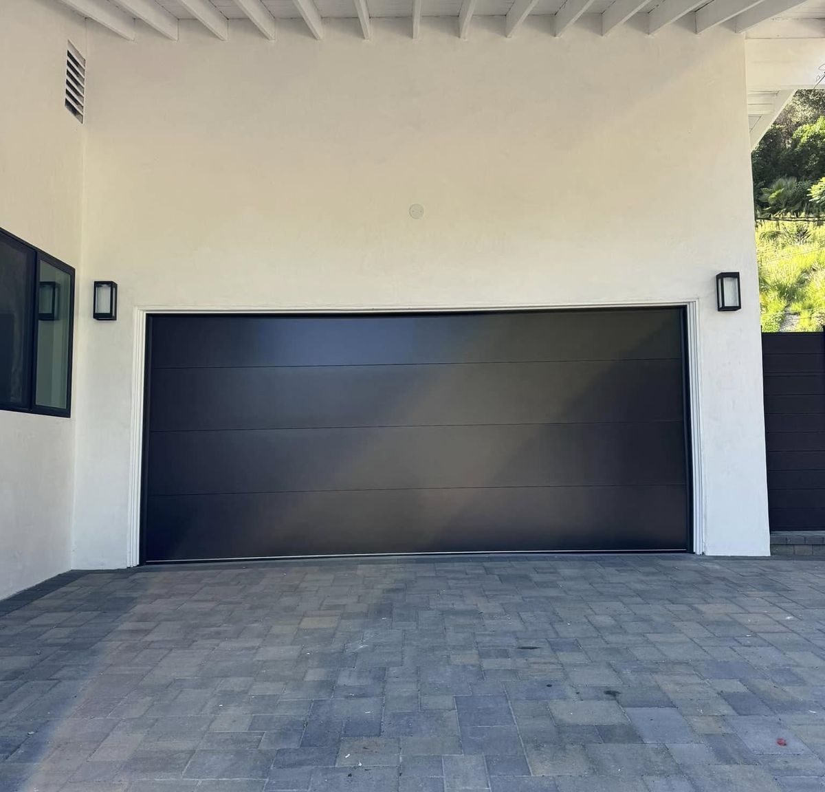 Black flush-panel modern garage door on a white contemporary Los Angeles home with a paver driveway