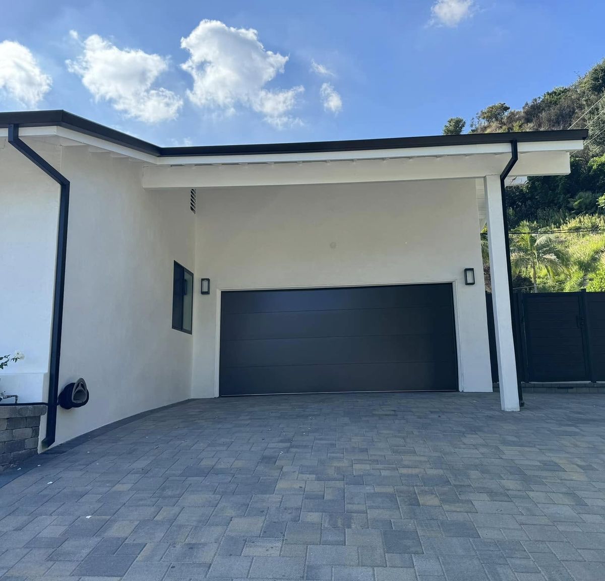 Dark gray flush-panel garage doors under a deep roof overhang on a modern Los Angeles home