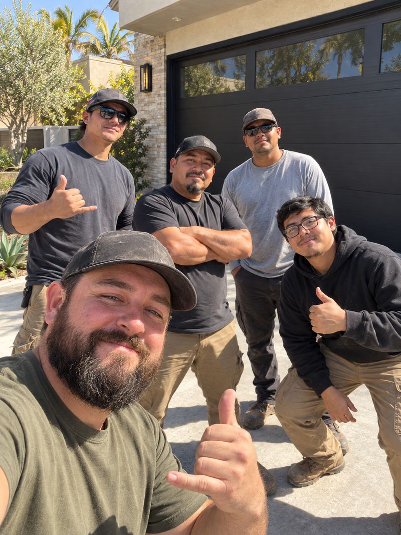 The Mighty Garage Doors crew taking a thumbs-up selfie in a driveway in front of a black garage door